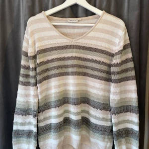 Randig tröja från Cappuccini - Säljer en randig tröja från Cappuccini i mjuka toner av beige, grön och vit. Tröjan har en v-ringad hals och långa ärmar. Den är stickad men är tunn och har en skön passform. 