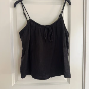 Svart linnetopp med knytband - Snygg svart linnetopp med justerbara axelband och knytband framtill. Perfekt för varma dagar och kan enkelt matchas med olika outfits.