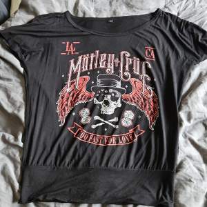 Cool svart t-shirt med Mötley Crüe-tryck. Designen har en dödskalle med hatt och röda vingar, samt texten 'Too Fast for Love'. Perfekt för rockälskare! Skön, luftig kvalitet. Inte mycket använd. Strl S. Köpt på EMP. Oversized med mudd längst ner som gör att den sitter snyggt.