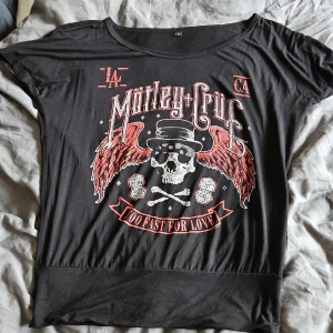 Svart Mötley Crüe t-shirt - Cool svart t-shirt med Mötley Crüe-tryck. Designen har en dödskalle med hatt och röda vingar, samt texten 'Too Fast for Love'. Perfekt för rockälskare! Skön, luftig kvalitet. Inte mycket använd. Strl S. Köpt på EMP. Oversized med mudd längst ner som gör att den sitter snyggt.