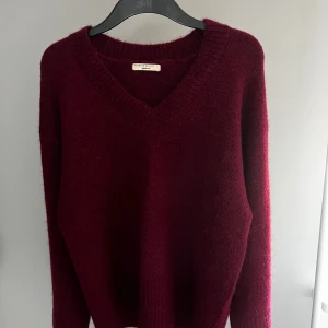 Vinröd stickad tröja från Gina Tricot - Mysig vinröd stickad tröja från Gina Tricot i storlek S. Tröjan har en v-ringad hals och långa ärmar, perfekt för kyligare dagar. Den är tillverkad i ett mjukt material som ger en skön känsla. Ett måste i garderoben för höst och vinter!