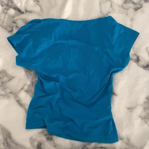 Blå kortärmad topp - Säljer en enkel och stilren blå kortärmad topp med öppen rygg. Perfekt för en avslappnad look. Toppen har en mjuk och bekväm passform.