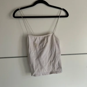 Vit ribbad linnetopp från Zara - Säljer en stilren vit ribbad linnetopp från Zara med tunna axelband. Perfekt för varma sommardagar eller som ett lager under en kavaj. Toppen har en enkel och elegant design som passar till många olika outfits.