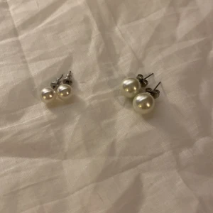 Pärlörhängen i silver - Säljer två par eleganta pärlörhängen med silverfäste. Perfekta för att ge en klassisk touch till din stil. Passar både till vardag och speciella tillfällen.