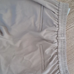 Beige byxor med resårmidja - Snygga beige byxor med resårmidja och stilrena fickor. Perfekta för en avslappnad look. Byxorna har en enkel design med raka ben och är gjorda i ett mjukt material för extra komfort. (Linneblandning) 