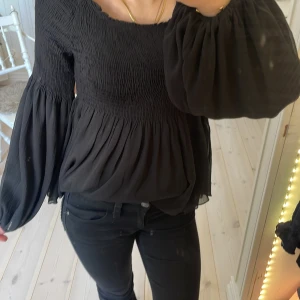 Svart blus från Lindex - Säljer en svart blus från Lindex med smockdetaljer och långa, vida ärmar. Blusen har en luftig passform och är tillverkad i tyll 💓