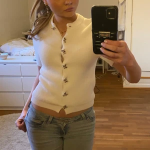 Vit kofta med rosett knappar - Säljer en stilren vit kofta med korta ärmar och rosett knappar framtill från Zara. Perfekt för en elegant look. Koftan har en rund halsringning och är kortärmad. Nypris: 379kr💕 köptes i höstas och säljer då den ej kommit till användning☺️ 
