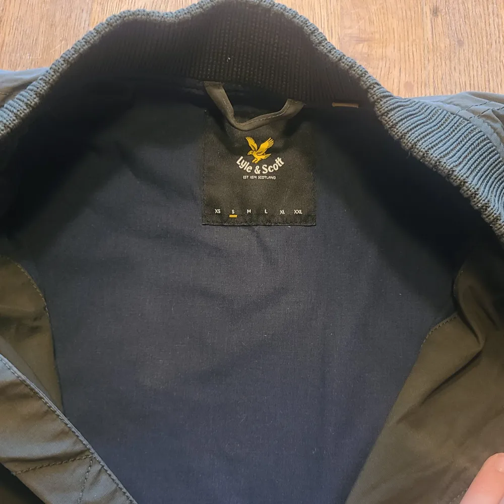 Säljer en snygg grön bomberjacka från Lyle & Scott. Jackan har en dragkedja framtill och ribbade muddar vid ärmslut och nederkant. Den ikoniska loggan syns på bröstet. Perfekt för en stilren look!. Takit.
