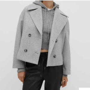 Grå kappa med knappar - Säljer en stilren grå kappa med dubbelknäppning och breda slag. Jackan har en kortare, boxig passform och är perfekt för höst och vår. Den är långärmad och tillverkad i ett mjukt material som ger en elegant look.