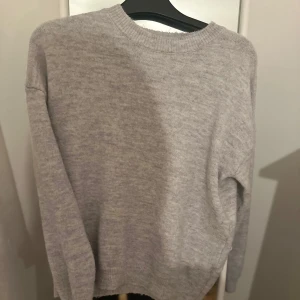 Grå stickad tröja från Gina Young - Säljer en mysig grå stickad tröja med rund hals och långa ärmar. Perfekt för kyliga dagar och enkel att matcha med olika outfits. Tröjan har en klassisk design med ribbstickade muddar vid ärmslut och nederkant. 