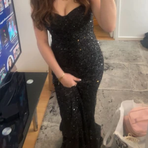 Svart glittrig långklänning - Säljer en elegant svart glittrig långklänning med en v-ringad design. Perfekt för festliga tillfällen. Klänningen har en figurnära passform som framhäver silhuetten.