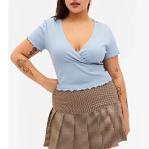 Ljusblå omlottopp - Säljer en ljusblå omlottopp med v-ringning och korta ärmar. Toppen har en ribbad struktur och en figurnära passform som framhäver midjan. Perfekt för en stilren och bekväm look. I xs