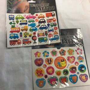 Tillfälliga tatueringar med fordon och djurmotiv - Två ark med tillfälliga tatueringar. Ett ark har färgglada fordon som bilar, bussar och skyltar. Det andra arket har söta djurmotiv i hjärtan och cirklar, inklusive katter, björnar och bin. Perfekt för barnkalas eller lekfulla tillfällen. 3 år +