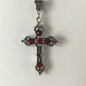 Silverfärgat korshalsband med röda stenar - Elegant korshalsband i silverfärg med detaljerade ornament och fem röda stenar. Perfekt för att ge en gotisk touch till din stil. Hängsmycket har en intrikat design som fångar ögat.