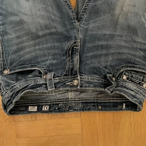 Blå jeans med broderade fickor från Miss Me - FÖRLÅT FÖR KONSTIGA BILDER. Vet inte varför dom ändrar håll. Säljer ett par snygga blå jeans från Miss Me med unika broderade detaljer på bakfickorna. Jeansen har en klassisk femficksdesign och en knappgylf. Dom är lite slitna där nere vid vaderna och det saknar några få diamanter på bakfickorna.