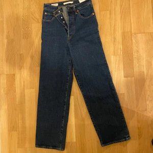 Mörkblå jeansbyxor från Levis - Snygga mörkblå jeansbyxor från Levis med klassisk design. Byxorna har en rak passform och är högmidjade med knappgylf. Perfekta för en stilren look. Rib cage straight W26