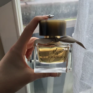 My Burberry Eau de Parfum - Säljer en elegant flaska av My Burberry Eau de Parfum. Flaskan rymmer 90 ml och har en stilren design med en beige rosett runt halsen och ett mörkt lock. Perfekt för den som älskar en klassisk och sofistikerad doft. Har ej boxen kvar!!!!