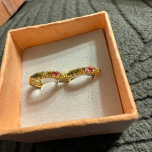 Guldörhängen med färgade stenar - Eleganta guldörhängen med flera färgade stenar i rött och grönt. Perfekta för att ge en färgglad touch till din stil. Kommer i en fin presentask.