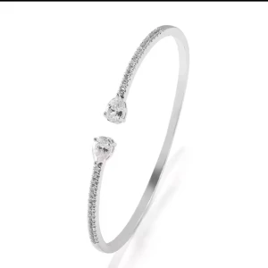 Glittrigt silverarmband med stenar - Ett elegant och tunt armband i silverfärg med glittrande små stenar längs ovansidan. Armbandet är öppet framtill och pryds av två droppformade stenar i varje ände för en lyxig och modern look.