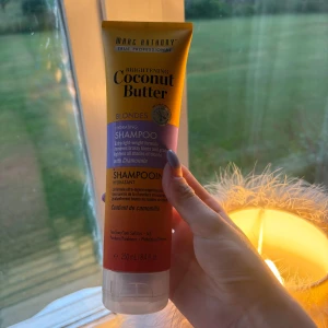 Marc Anthony Coconut Butter Shampoo - Brightening Coconut Butter Hydrating Shampoo för blont hår med kamomill. Kommer i en tub på 250 ml i gult, lila och orange. Sulfat- och parabenfri formula som tar bort gula toner och ger fukt till håret. Perfekt för dig som vill ha ljusare och fräschare blonda nyanser.