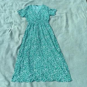 Grön blommig maxiklänning från SHEIN - Snygg långklänning i grönt med vitt blommigt mönster. Klänningen har korta ärmar, v-ringning och markerad midja. 