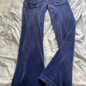 Blå velourbyxor Juicy Couture XS - Mysiga blå velourbyxor från Juicy Couture i storlek XS. Byxorna har bred resår i midjan, två fickor med lock och tryckknappar bak. Perfekta för en chill och trendig look.