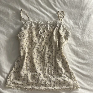 Blommig spetslinnetopp med rosett - Supersöt ljusbeige linne-topp med små blå blommor, tunna axelband och spets detaljer💚