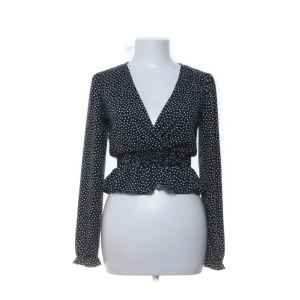 Svart prickig blus från Bershka - Supersöt svart blus från Bershka med vita prickar, v-ringning och smockad midja som ger en snygg volangkant. Långärmad modell i lätt och luftig polyester, perfekt för dig som gillar trendiga detaljer och en feminin look. Det är bara att skriva om ni har några frågor💕💕