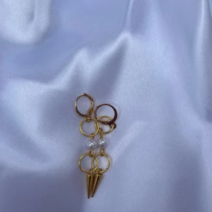 Guldiga örhängen med pärlor och spikes - Unika örhängen i guldton med flera ringar, 1 vit pärla och coola konformade spikes. Perfekt accessoar för dig som vill sticka ut med en edgy och trendig stil.
