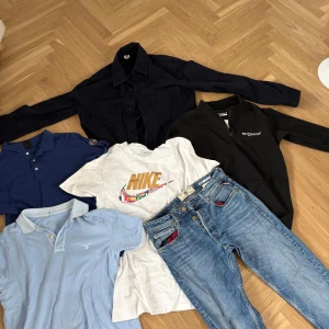 Klädpaket herr – Nike, GANT, jeans  - Säljer ett helt paket med snygga herrkläder i bra skick. Perfekt för någon som gillar stilrena och sportiga plagg! Paketet innehåller: – Nike T-shirt med flagg-swoosh (S) – GANT pikétröja ljusblå (S) – Marinblå piké (okänt märke) (M) – Svart halvzip för träning (S) – Mörkblå skjortjacka (50) – Blå jeans med röda fickdetaljer & dubbelknäppning (REPLAY) (30,32)
