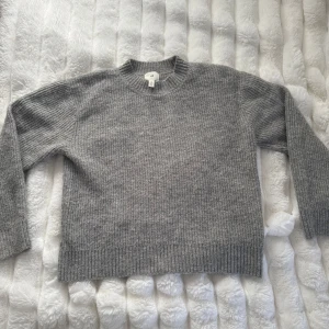 Grå stickad tröja från H&M - Mysig grå stickad tröja från H&M med rund halsringning och ribbade muddar. Perfekt för lager-på-lager och passar till både jeans och kjol. Långärmad och i klassisk modell som funkar året runt.