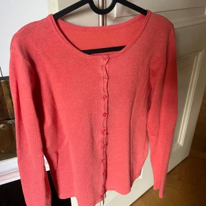 Korallrosa kofta med knappar - Snygg korallrosa kofta med rund halsringning och knäppning framtill. Långärmad och i mjukt, stickat material som känns skönt mot huden. Perfekt att slänga över en t-shirt eller linne för en chill look. Finns ingen lapp eller tvättråd, så vet detför inte vilket märke eller storlek, därav priset 🩷