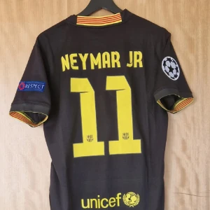 FC Barcelona tröja  - Snygg FC Barcelona fotbollströja med Neymar Jr och nummer 11 på ryggen. Svart med gula detaljer, officiella Champions League och Respect-patchar på ärmarna. Broderad klubbmärke och Nike-logga, Qatar Airways-tryck på bröstet. Tillverkad i ventilerande polyester. Den användes under säsong 13-14 och har top kvalitet för är använd en gång 
