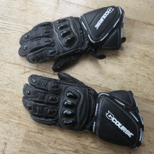Course Alpha Sport MC-Handskar - Säljer ett par svarta motorcykelhandskar från Course, modell Alpha Sport Glove. Handskarna har förstärkta knogar, vita kontrastsömmar och breda muddar med Course-logga. Tillverkade i slitstarkt skinn med extra grepp i handflatan och justerbar kardborre vid handleden.