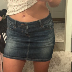 Mörkblå jeanskjol med fickor - Säljer en klassisk mörkblå jeanskjol med fem fickor och bälteshällor. Kjolen är kort och har en snygg tvättad look med synliga sömmar. Perfekt för dig som gillar en enkel men trendig stil. Från Lbt 