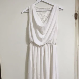 Vit långklänning med spetsdetaljer - Elegant vit långklänning med djup v-ringning och vackert draperat liv. Baksidan har transparent spets med blommönster som ger en romantisk känsla. Klänningen är ärmlös och har resår i midjan för en bekväm passform. Perfekt för speciella tillfällen🤍                                   DET ÄR ONE SIZE OCH PASSAR OM MAN HAR STORLEK S ELLER M.