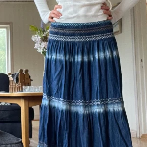 Blå långkjol med broderade detaljer - Supersnygg blå långkjol med broderade vågiga detaljer och smock i midjan. Kjolen har flera volanger och ett coolt batikmönster i vitt. Nypris på 600kr😋🫶 