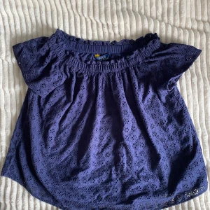 Mörkblå blus från Polo Ralph Lauren - Supersöt mörkblå blus från Polo Ralph Lauren med broderade blommor och offshoulder-modell. Blusen har korta ärmar och resår upptill för en snygg passform. Perfekt för dig som gillar romantiska detaljer och vill ha en luftig topp i bomull. Kommer från ett hem med katt. Hör gärna av dig om du har några frågor.