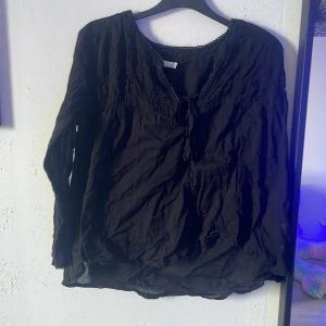 Svart blus med knytning Vintage M - Svart blus från Vintage i storlek M. Lätt och luftig med långa ärmar, knytning vid halsen och diskret spetskant runt kragen. Perfekt för dig som gillar en avslappnad men ändå stilren look.