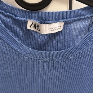 Blå ribbad topp från Zara - Säljer en blå ribbad topp från Zara i storlek L. Toppen har rund halsringning och halvlånga ärmar. Den är figurnära och stretchig, perfekt för dig som gillar en enkel men snygg stil. Passar till både jeans och kjol.