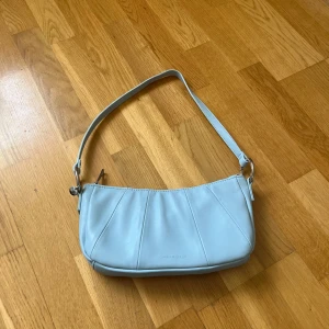 Ljusblå axelväska från Carin Wester - Snygg ljusblå axelväska från Carin Wester i slät syntet med silverfärgade detaljer. Väskan har dragkedja upptill, innerfack och stilrena sömmar framtill. Perfekt storlek för det viktigaste och en clean look som passar till många outfits.