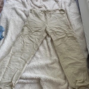 Beiga linnebyxor från Kappahl - Snygga och luftiga beiga linnebyxor från Kappahl i storlek 158. Byxorna har resår i midjan och raka ben, perfekta för en chill och avslappnad stil. Tillverkade i ett skönt linnematerial som passar bra när det är varmt ute.