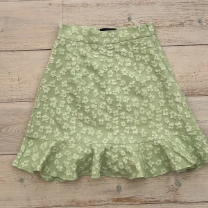 Grön blommig kjol från Pieces - Supersöt ljusgrön kjol från Pieces med 3D-blommor och volangkant nertill. Kjolen har en A-linjeformad siluett och är perfekt för vår och sommar. Blommönstret ger en romantisk vibe och materialet känns mjukt och lätt.