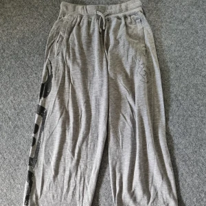 Grå mjukisbyxor från GASP M - Grå mjukisbyxor från GASP med stort tryck längs benet och logga framtill. De är uppsydda (fastklistrade)  intill så längd går att justera lite. Liten defekt på benet