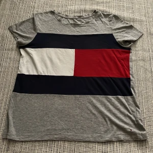 Grå t-shirt Tommy Hilfiger - Snygg grå t-shirt från Tommy Hilfiger med breda block i vitt, rött och marinblått framtill. 