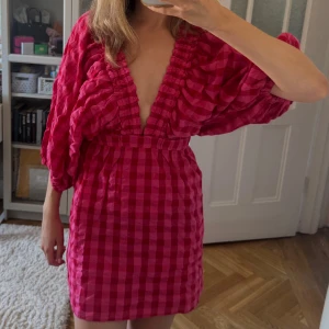 Rutig rosa kortklänning Gina Tricot - Superfin kort rutig klänning i  rosa från Gina Tricot. Djup v-ringning (som går att göra mindre eftersom man kan knäppa den - se bild 3), puffiga trekvartsärmar och markerad midja. Lätt och luftig, perfekt för varma dagar. Snygg struktur och cool volym i ärmarna. Helt oanvänd och prislappen finns kvar!❤️🩷❤️🩷💐