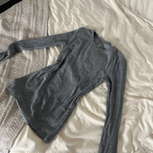 Grå ribbad långärmad tröja S - En enkel och stilren grå långärmad tröja i ribbat material. Tröjan har rund halsringning och en slim passform som sitter snyggt på kroppen. Perfekt att bära som basplagg eller under en hoodie. Supermjuk och skön mot huden.