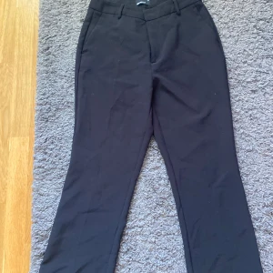 Svarta kostymbyxor från Gina Tricot - Svarta kostymbyxor från Gina Tricot i klassisk rak modell. Byxorna har hällor för bälte, diskreta fickor bak och är tillverkade i ett mjukt tyg som känns skönt mot huden. Perfekta för en clean och stilren look. Priset kan diskuteras.