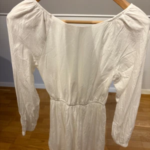 Vit långärmad klänning med öppen rygg - Superfin vit klänning med långa ärmar och markerad midja. Klänningen har en snygg öppen rygg och är gjord i ett mjukt bomullstyg.