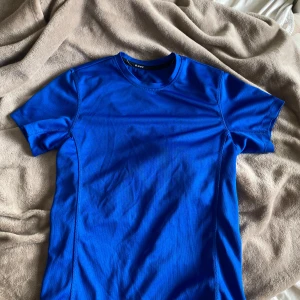 Blå tränings-tshirt från SOC - Sportig blå t-shirt från SOC i funktionsmaterial, perfekt för träning. Modellen är kortärmad med rund halsringning och har en clean, enkel design utan mönster. Materialet är lätt och andas, vilket gör den skön att ha på sig under aktiva dagar. Pris kan diskuteras.